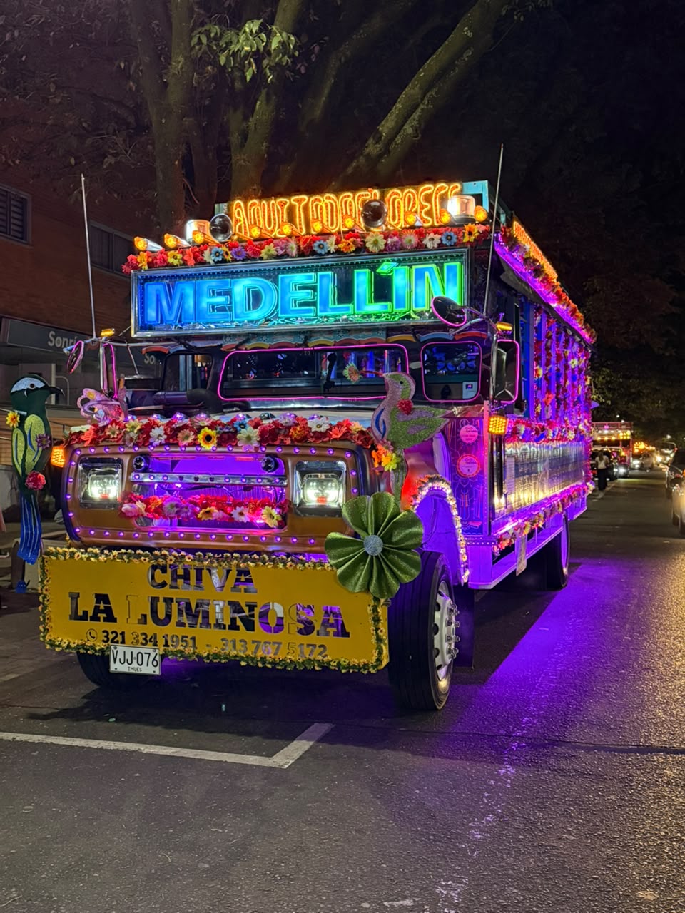 La segunda Chiva La Luminosa de noche, con luces moradas y el letrero de Medellín